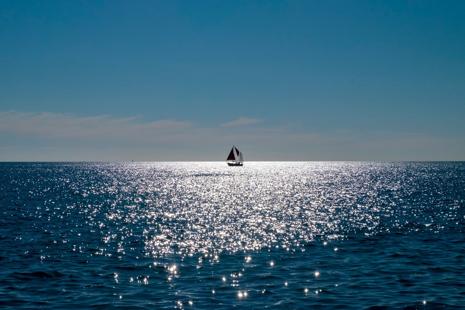 Sailboat on the sparkling blue ocean under clear sky